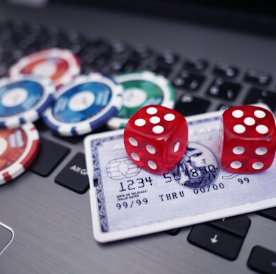 A set of red dice and poker chips are placed on top of a credit card, which is situated on a laptop keyboard. The poker chips are in various colors, including blue, green, red, and white.