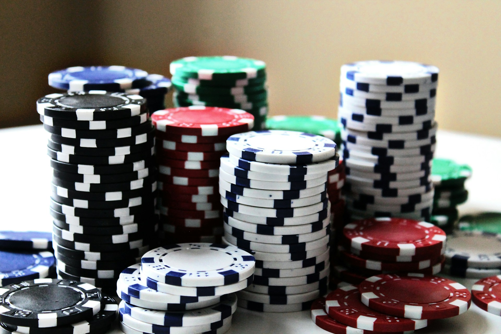 Stacks of colorful poker chips are arranged in piles on a white surface. The chips are blue, red, green, black, and white, each color having distinct markings.